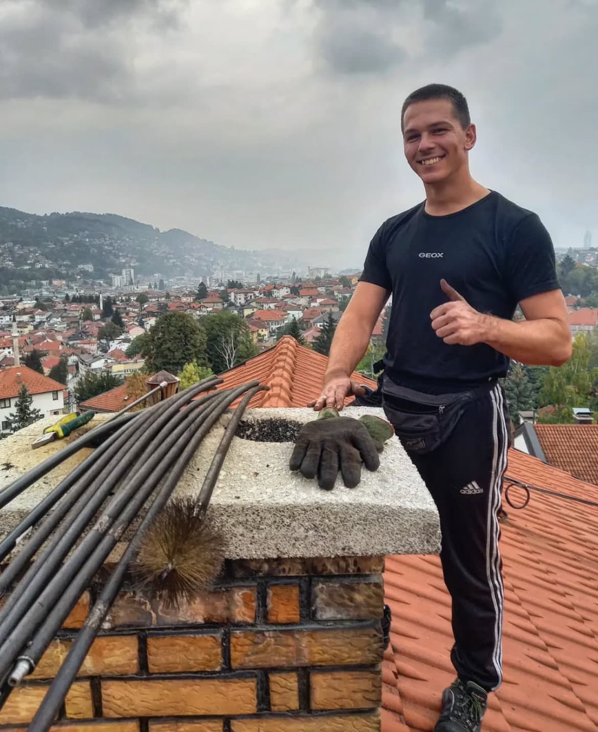 Dimnjačar Brkić na krovu u Sarajevu — panorama grada sa dimnjacima